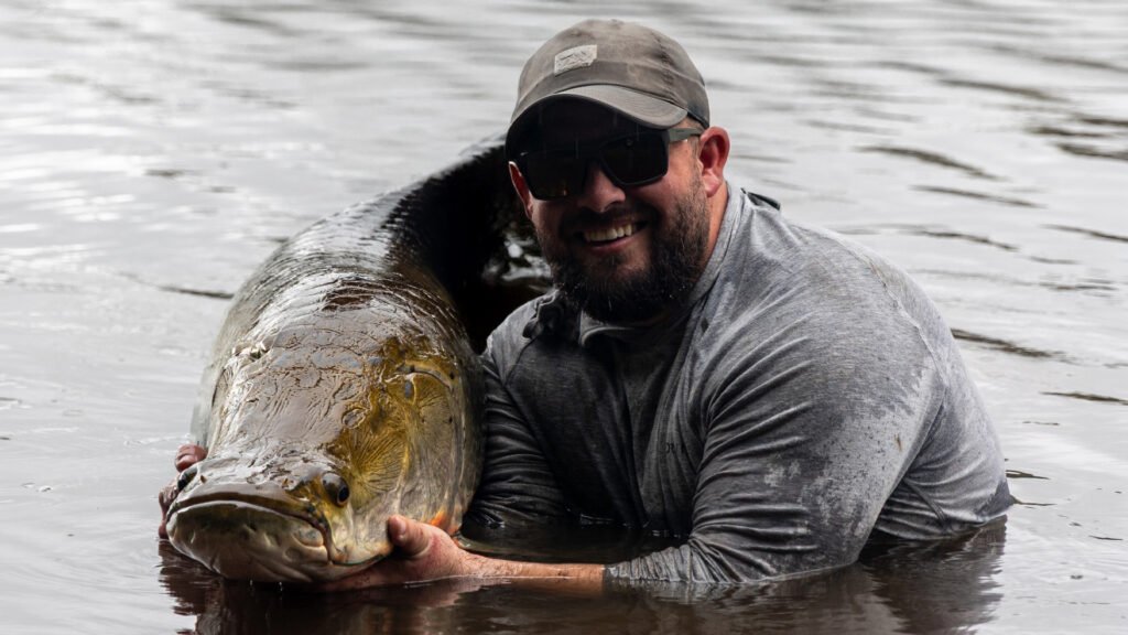 An angler kneels next to a large Arapaima.