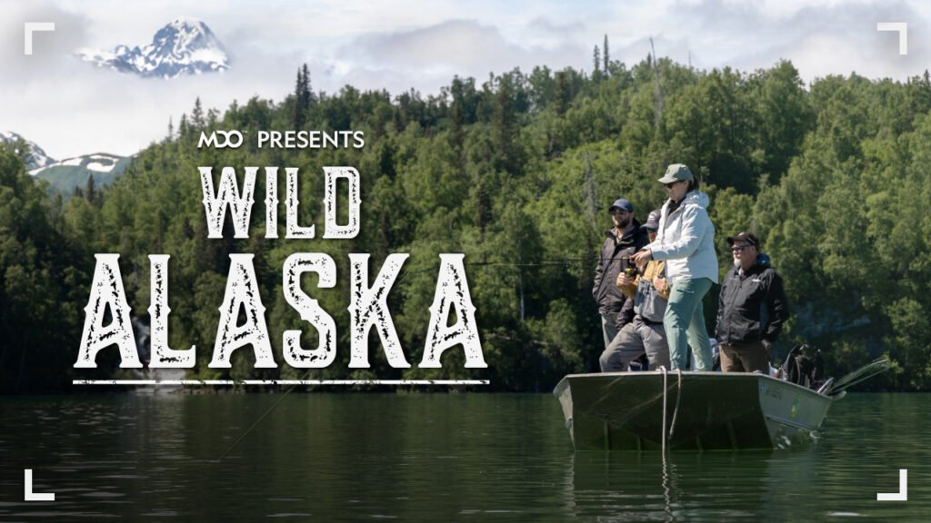 Anglers fish from a boat with a beautiful mountain/forest background. Text reads, "MDO presents, Wild Alaska."