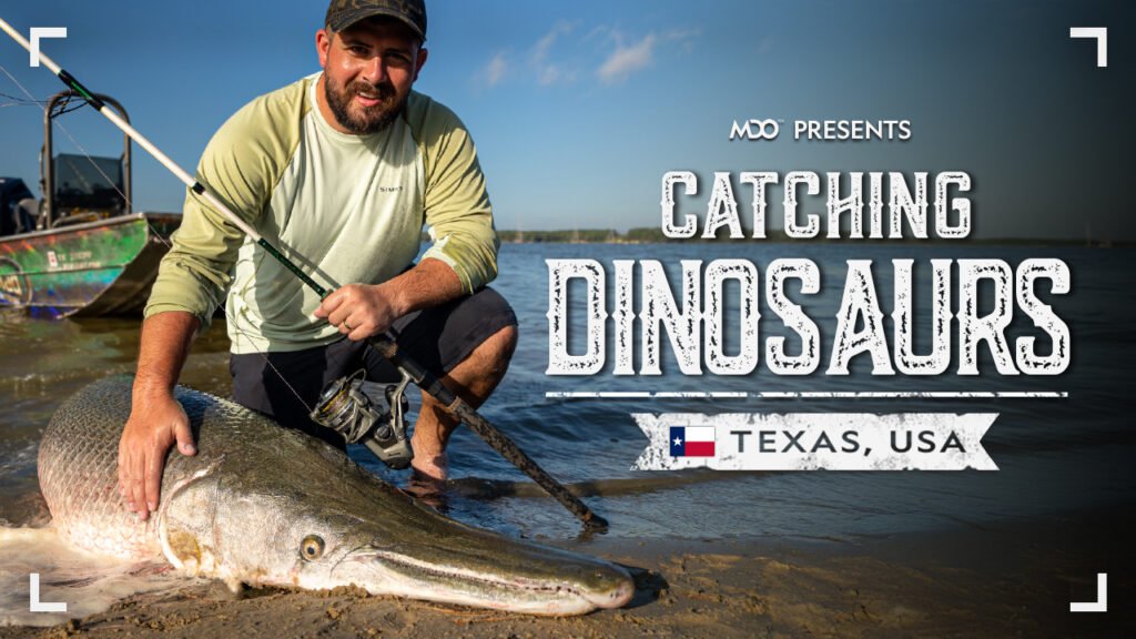 Bo poses with a large, Alligator Gar. Text reads, "MDO presents, Catching Dinosaurs, Texas USA"